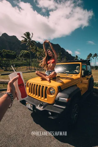 Woman posing on a yellow Jeep with palm trees and mountains in Hawaii