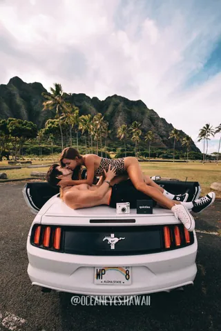 Couple kissing on a white convertible with Hawaii mountains behind
