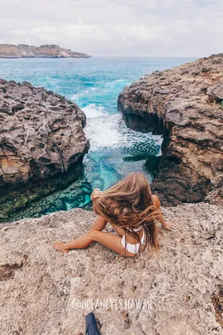 Woman sitting by a turquoise ocean inlet among rocks in Hawaii