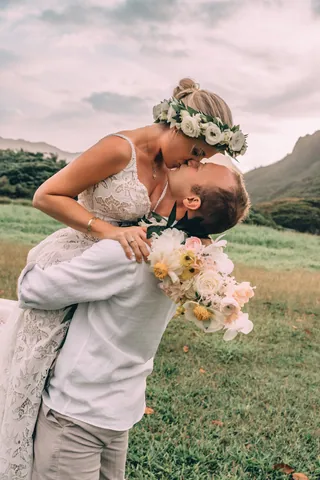 Groom lifting the bride for a kiss on a green meadow in Hawaii