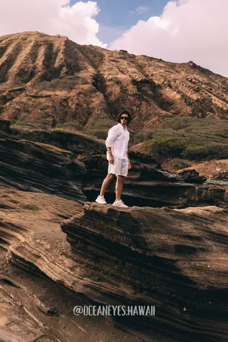 Man in white standing on layered lava rocks in Hawaii