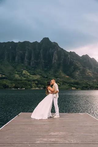 Wedding couple kissing on a pier with mountains in Hawaii