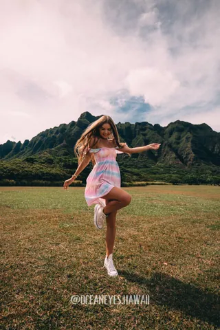Woman in a pink dress jumping on a meadow with mountains in Hawaii