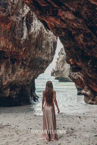 Woman in a long dress at a sea cave arch in Hawaii