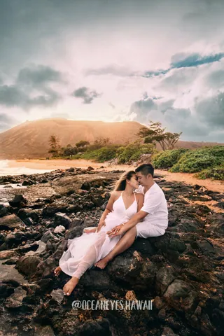 Couple sitting on lava rocks by the ocean in Hawaii