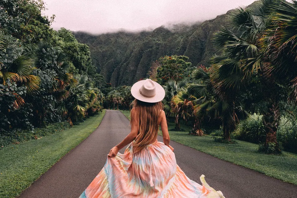 Woman in a hat walking down a palm-lined road in Hawaii