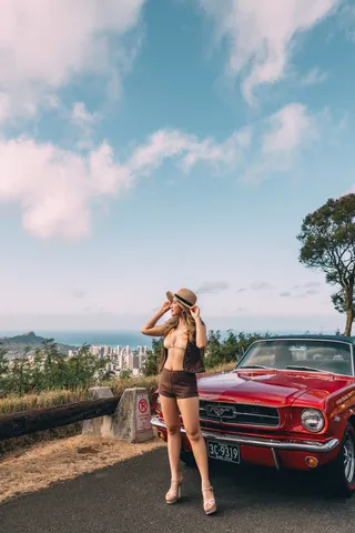 Woman posing by a red vintage Mustang overlooking Honolulu